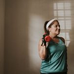 Middle-aged woman in workout attire lifting a dumbbell indoors, promoting fitness and healthy lifestyle.